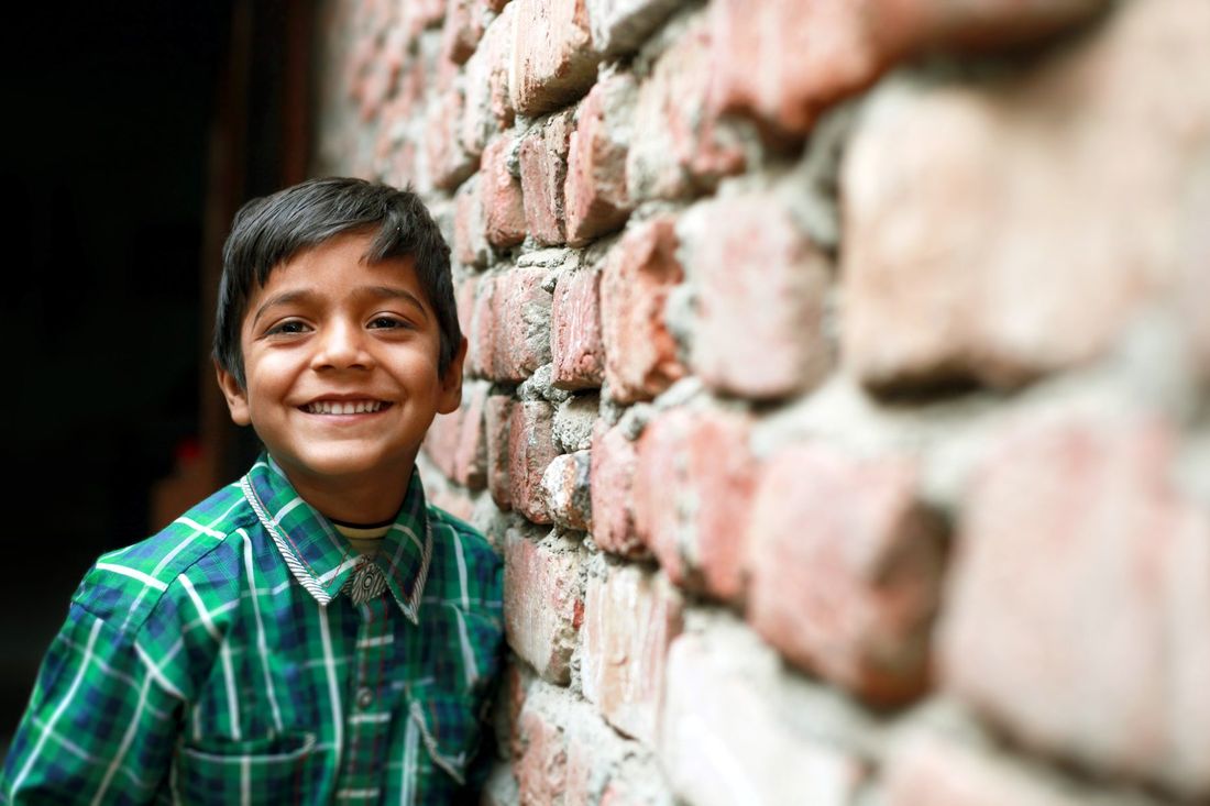 A smiling child beside a brick wall